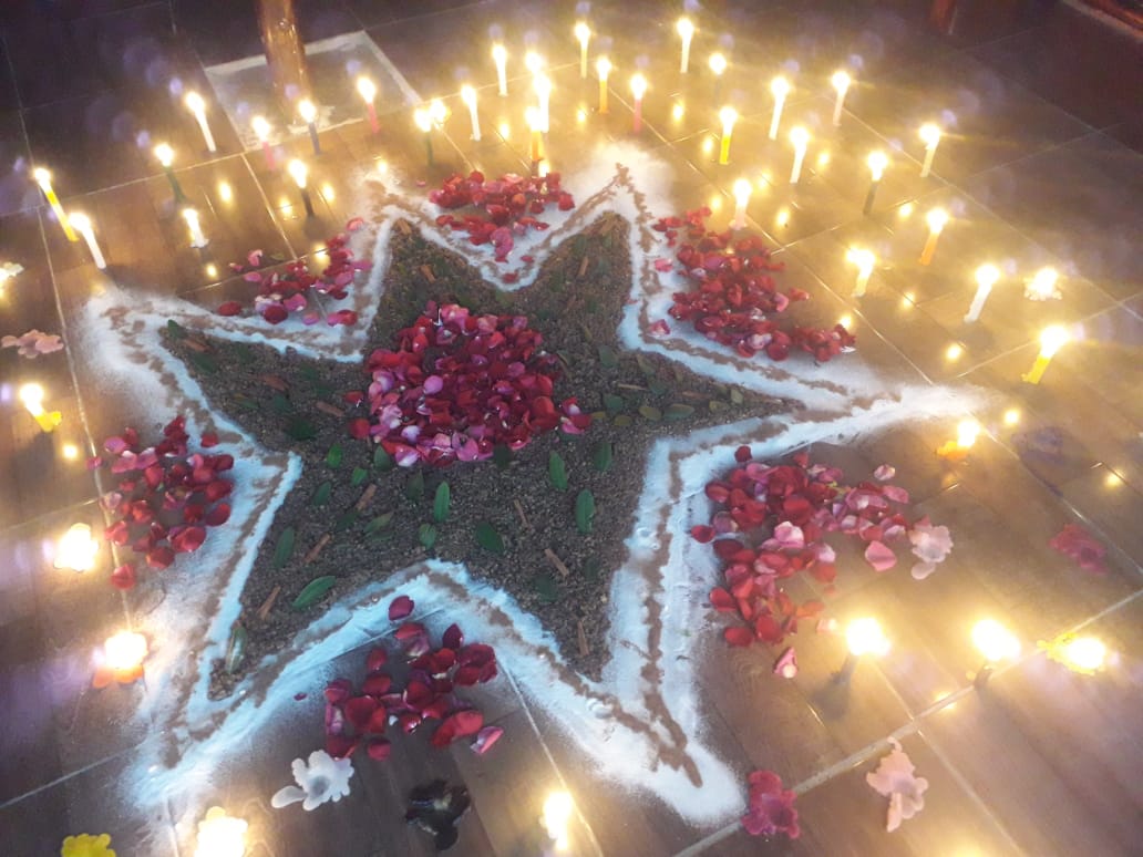 Estrela ritual desenhada no chão com velas acesas e pétalas vermelhas.
