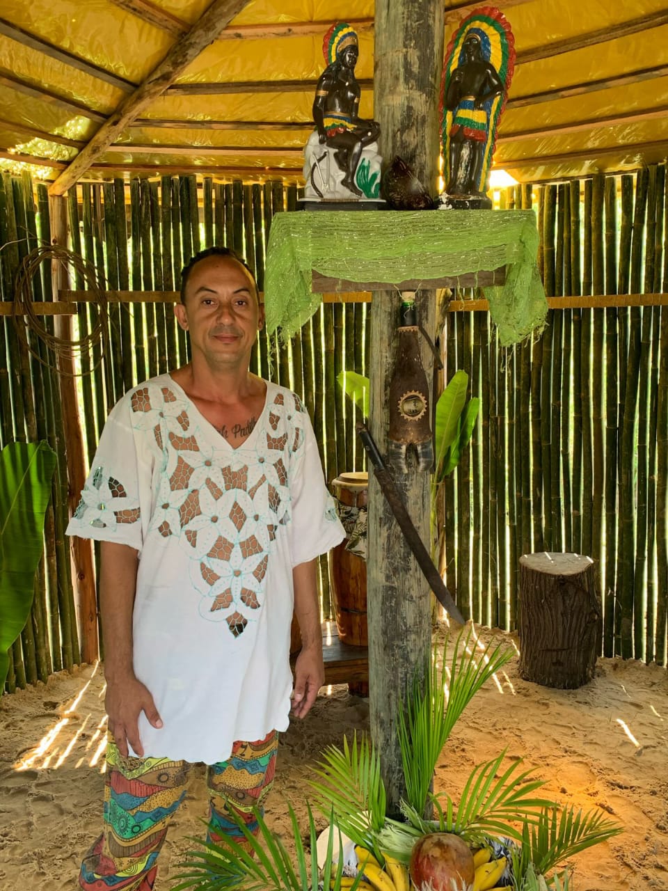 Pai Rodrigo em espaço sagrado da casa com madeira, areia e símbolos ancestrais.